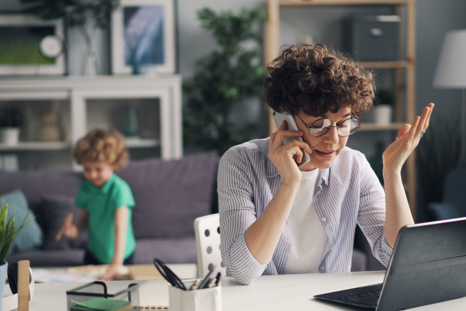 Mother taking a work call at home while her child plays in the background