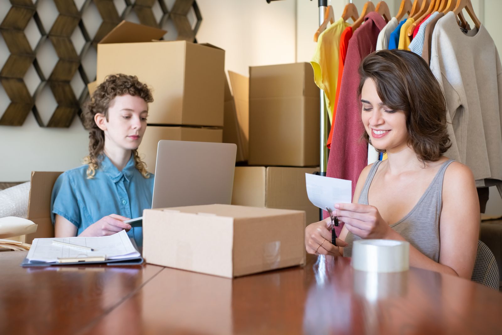 Two women managing online product orders with packing boxes and a laptop